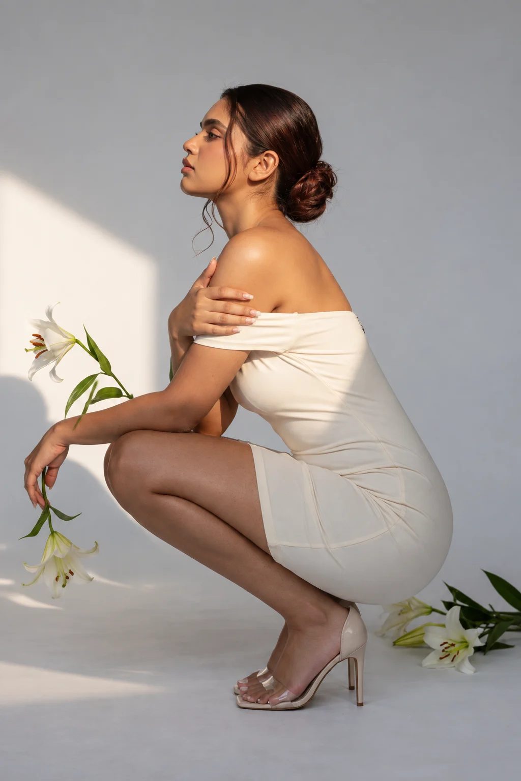 Full-body fashion illustration of a model crouching in a cream off-shoulder short dress, holding white lilies